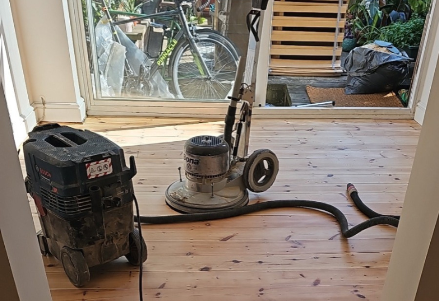 Wood Floor Sanding in south-west-london — dust-free buffing of solid softwood pine floorboards with a Bona buffer and HEPA extractor near patio doors.