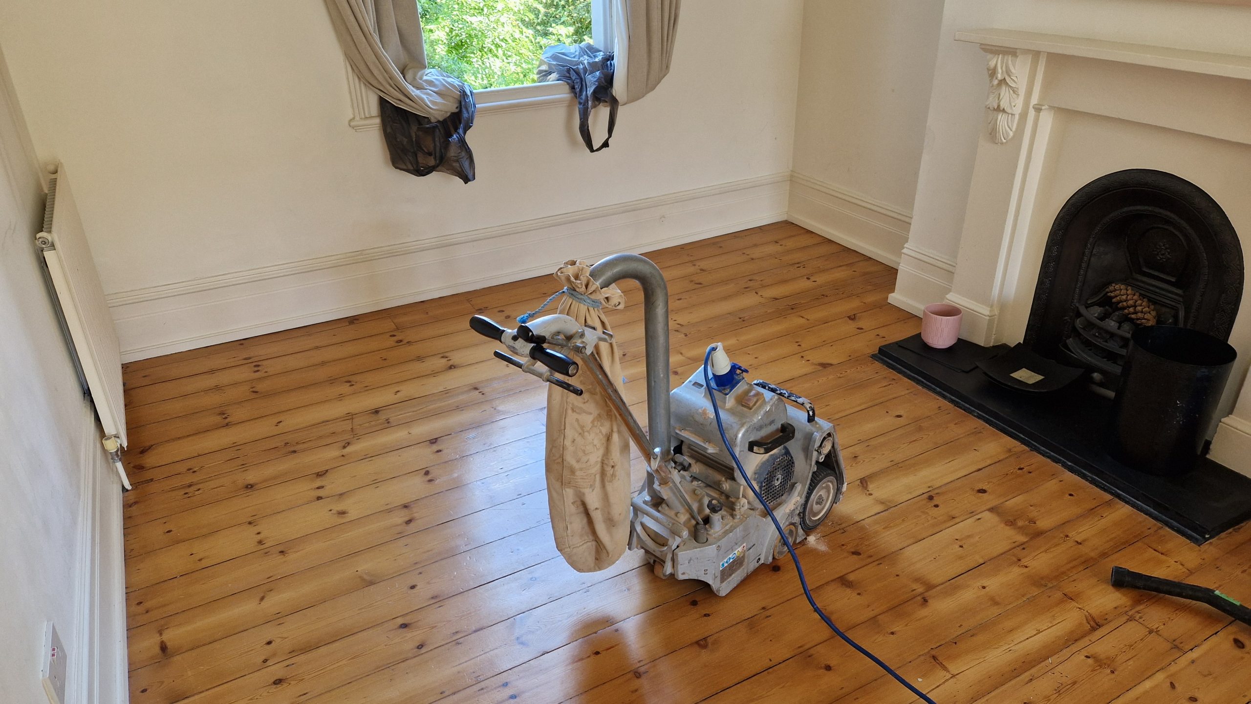 Wood Floor Sanding South-West London – Softwood Pine Floorboards Restored Dust-Free Wood Floor Sanding in south-west-london: dust-free drum sander restoring softwood pine floorboards in a bright Victorian room with fireplace and sash window.