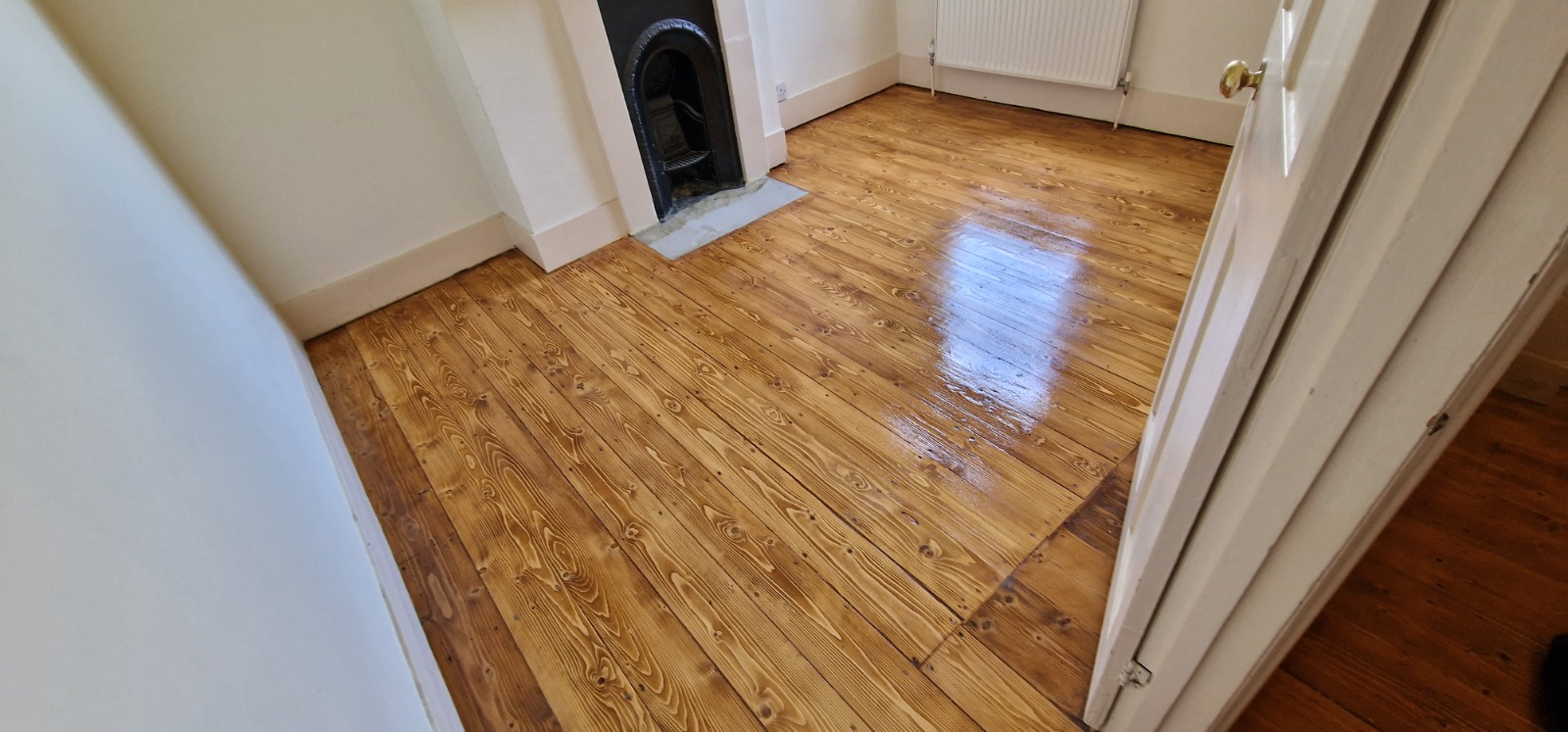 Wood Floor Sanding in south-west-london — Victorian softwood pine floorboards freshly restored, with a clear coat curing and a cast-iron fireplace in view.