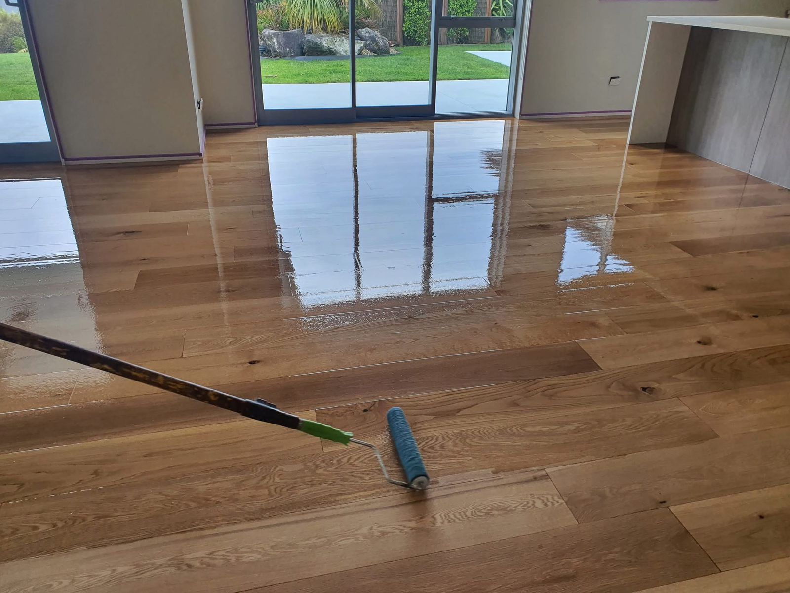 Hardwood Floor Refinishing in south-west-london – engineered oak hardwood planks being rolled with a clear lacquer for a smooth, durable finish in a bright living room.