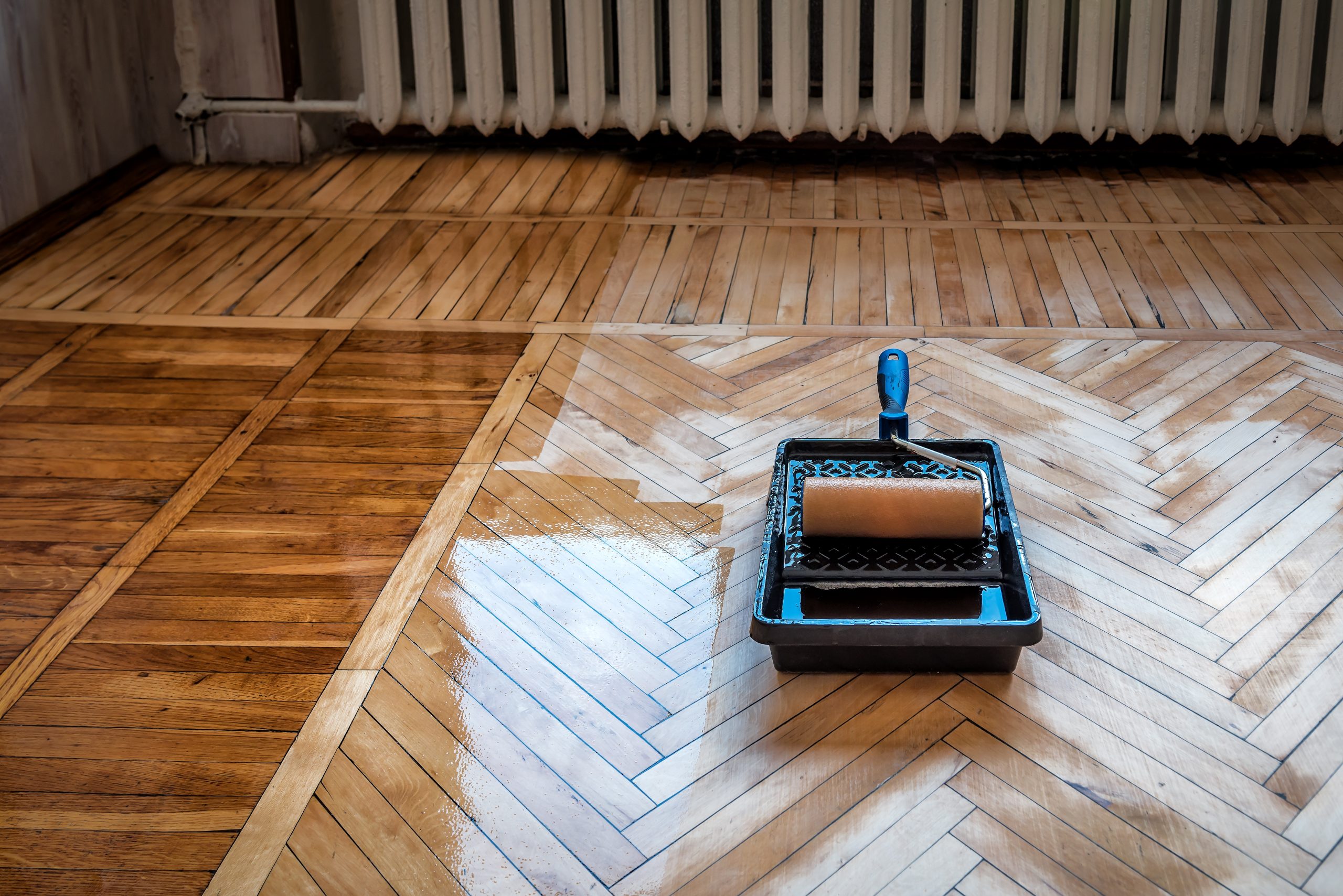Hardwood Floor Refinishing in south-west-london – oak herringbone parquet being lacquered with a roller tray, showing contrast between sanded wood and freshly sealed glossy finish.
