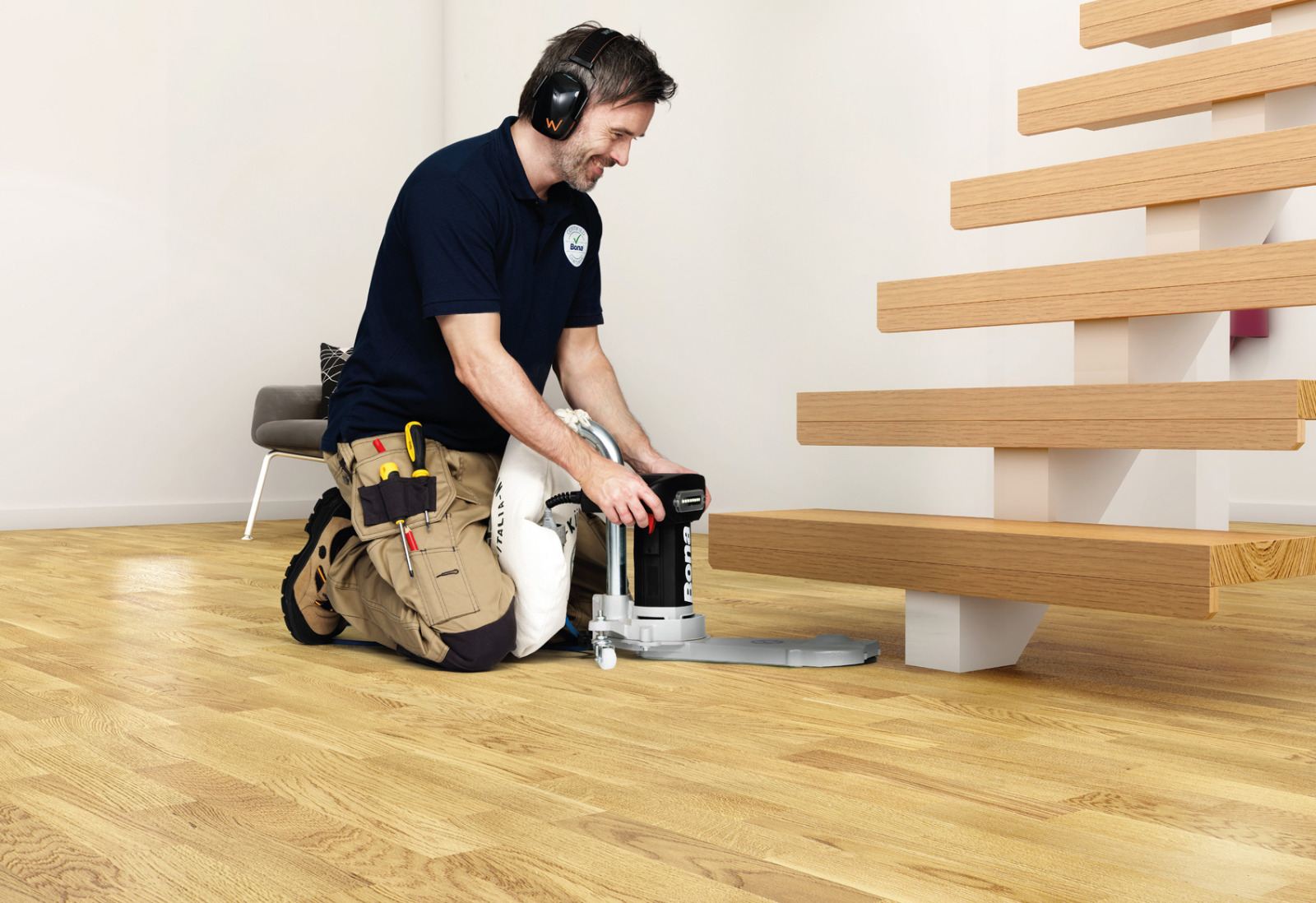 Hardwood Floor Refinishing in south-west-london – technician edge-sanding an oak mosaic parquet hardwood floor beside a staircase to prepare for a smooth, durable finish.