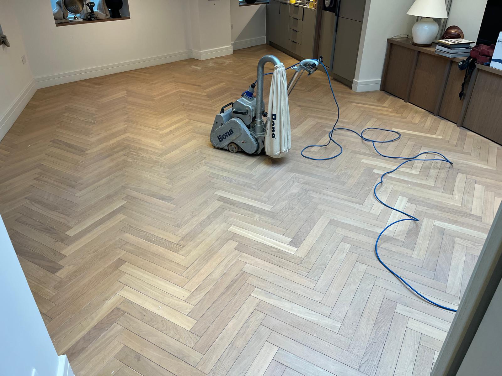 Parquet Floor Sanding in south-west-london on a light oak herringbone parquet floor, mid-sanding with a professional Bona machine in a modern living room.