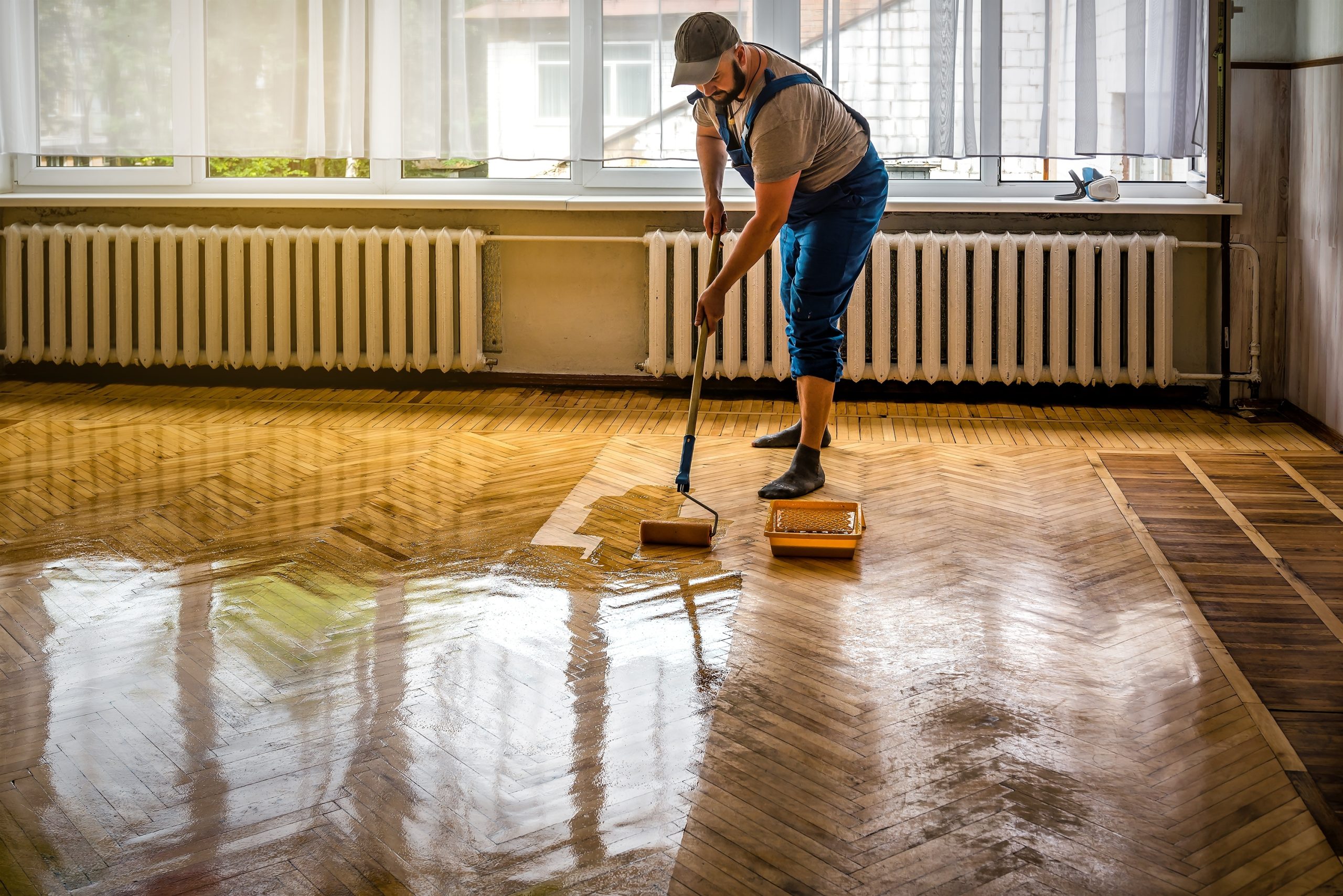 Parquet Floor Sanding in south-west-london, technician applying lacquer to an oak herringbone parquet floor, creating a glossy, freshly restored finish.