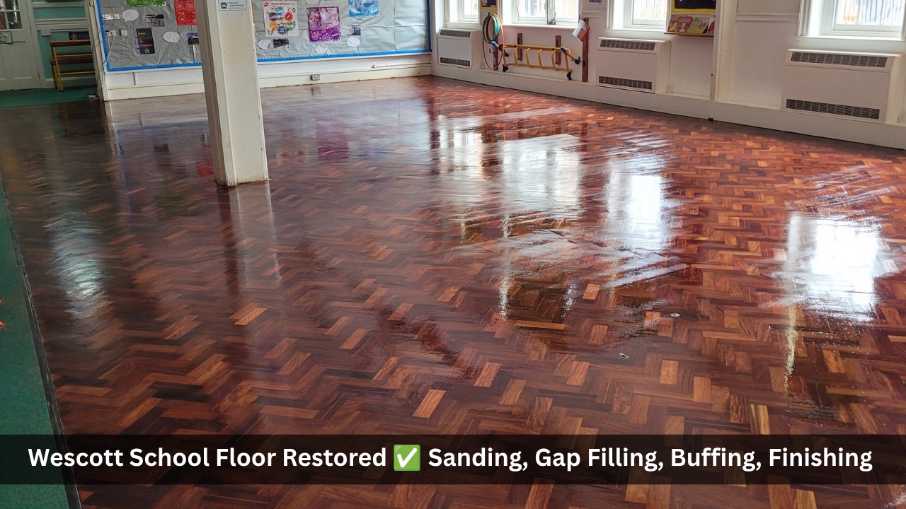 Fully restored dark oak parquet herringbone floor in a school hall after professional sanding, gap filling, buffing and finishing, showing a high-gloss reflective surface